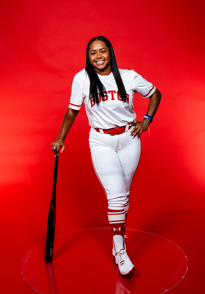 Boston University Women's Softball player Kyomi Apalit in her uniform with a bat in her hand. 